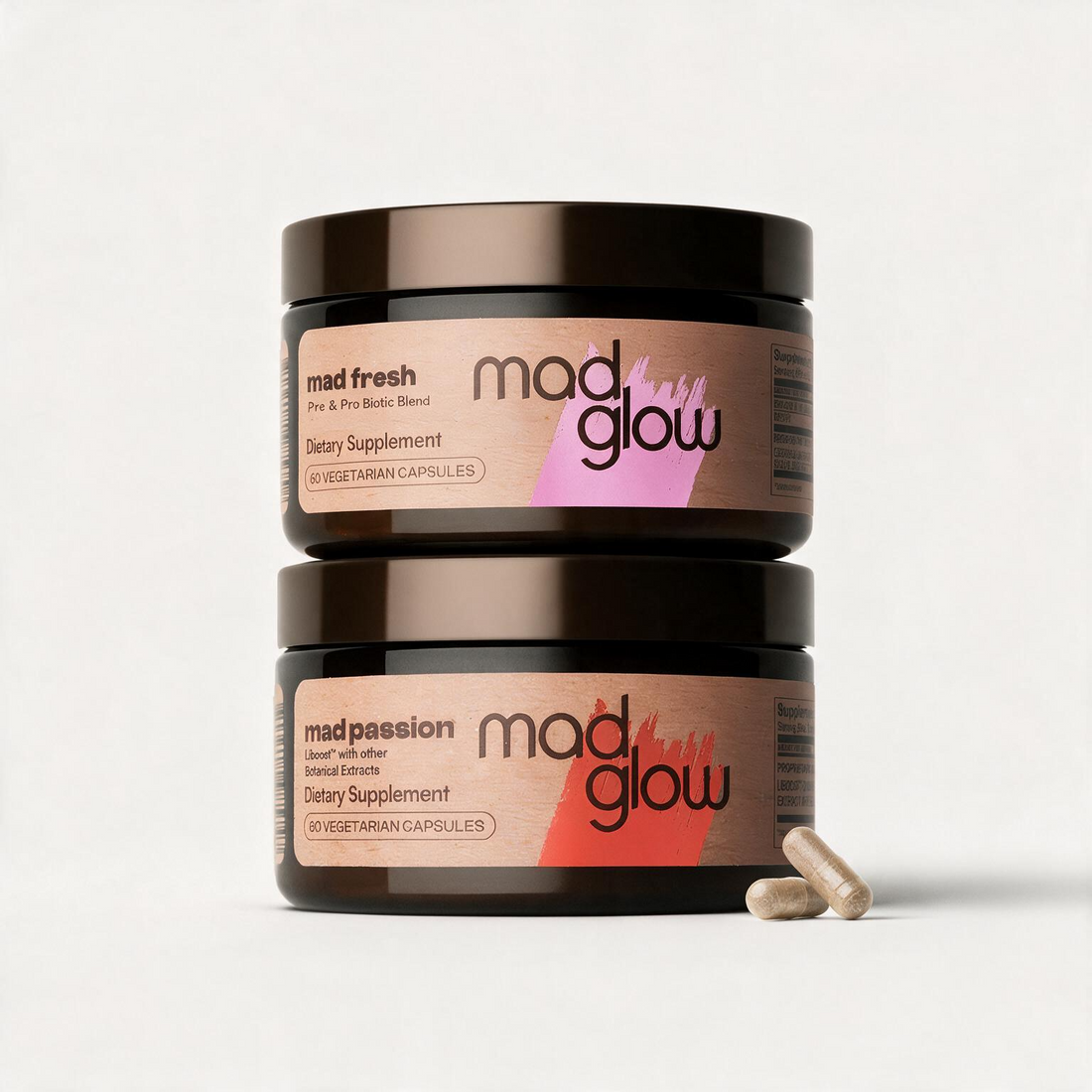 Two stacked dark amber supplement jars on a light gray background, with two capsules in front. The top jar label reads &